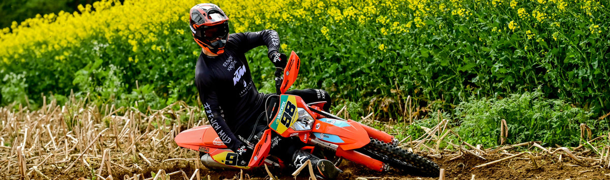 Pilote French Mud en enduro dans un virage devant un champ de colza